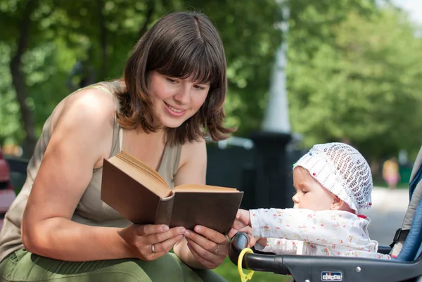 Mãe lê um livro de sua filhinha no parque — Fotografia de Stock