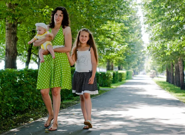 Woman and two children walking down the avenue in the park — Stock Photo, Image