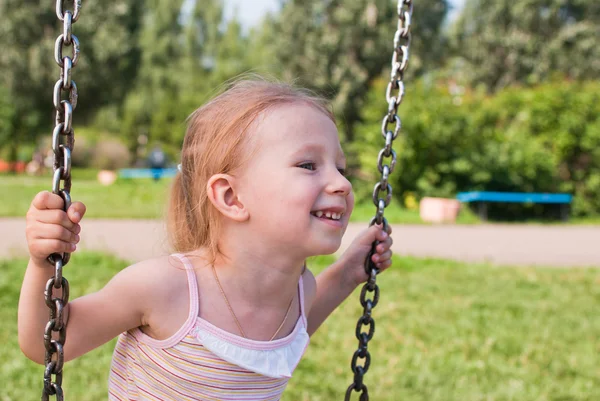 Kleines Mädchen schaukelt auf einer Schaukel und lächelt — Stockfoto
