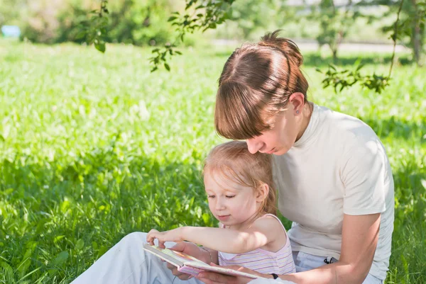 Мать и дочь сидят на траве и смотрят книгу — стоковое фото
