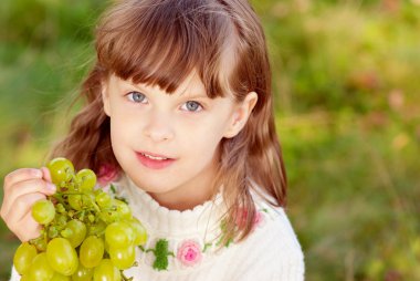 Small beautiful girl eats green grapes clipart