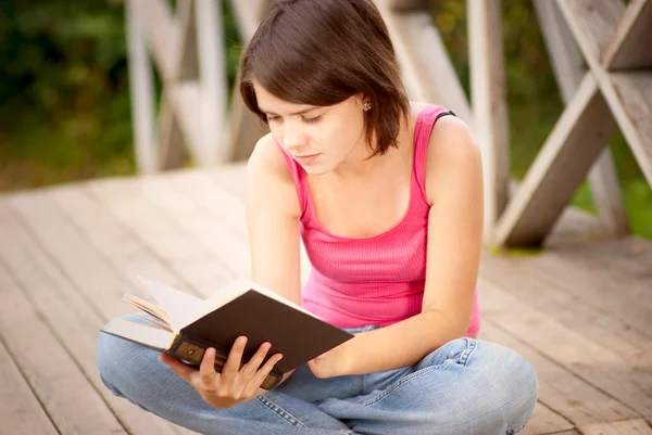 Genç güzel kız köprüsü üzerinde oturur ve kitap okuma — Stok fotoğraf