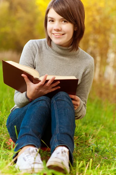 Mooi meisje zit op brug en boek leest — Stockfoto
