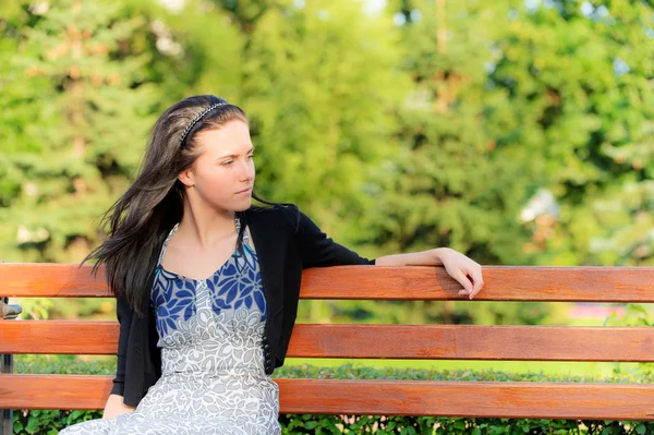 Krásná bruneta sedí na lavičce — Stock fotografie
