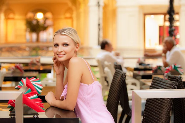 Menina sorridente senta-se em pequena mesa no restaurante — Fotografia de Stock