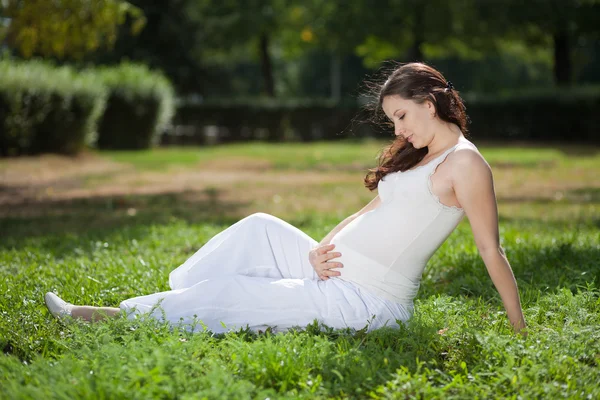 Çayır üzerinde oturan hamile kadın — Stok fotoğraf