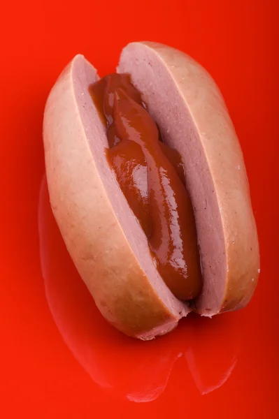 Ковбаса з кетчупом на червоному — стокове фото