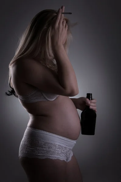 Беременная женщина с бутылкой алкоголя и сигаретой — стоковое фото