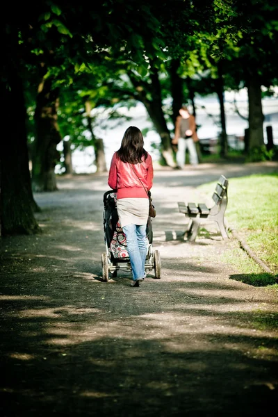 Woman walking with baby carriage in park — Stock Photo, Image