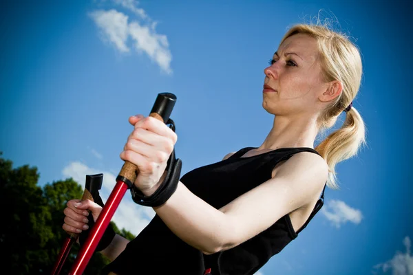 Nordic-walking - jonge vrouw is wandelen tegen blauwe hemel. — Stockfoto
