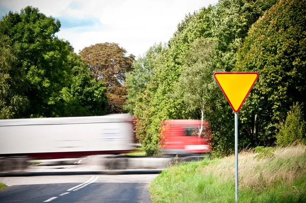 Opbrengst teken in de buurt van kruispunt en haasten vrachtwagen — Stockfoto