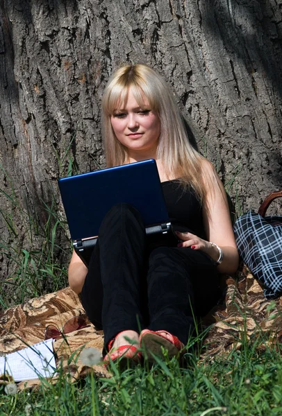 A menina agradável nova com o computador portátil no parque — Fotografia de Stock