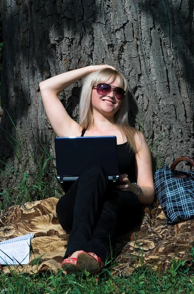 A menina agradável nova com o computador portátil no parque — Fotografia de Stock