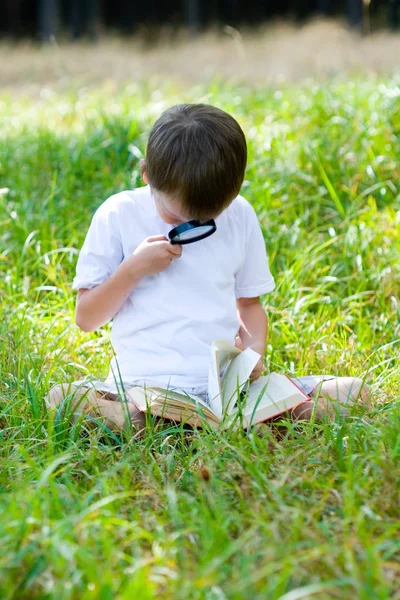Happy boy with a magnifying glass and a book — Stock Photo, Image