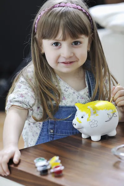 Schattige kleine meisje schilderij piggy bank — Stockfoto