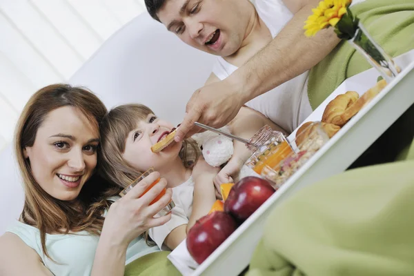 Šťastná mladá rodina jíst snídani v posteli — Stock fotografie