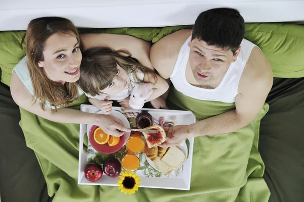 Счастливая молодая семья завтракает в постели — стоковое фото