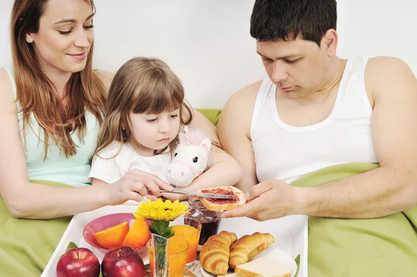 Glad ung familj äter frukost på sängen — Stockfoto