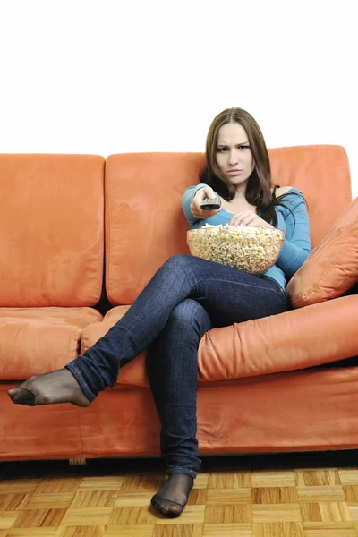Mujer joven come palomitas de maíz en sofá naranja —  Fotos de Stock