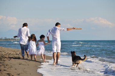 Mutlu bir aile sahilde köpekle oynuyor.