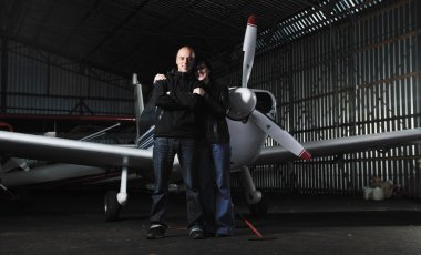 Happy young couple posing in front of private airplane clipart