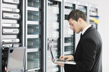 Young it engeneer business man with thin modern aluminium laptop in network server room clipart