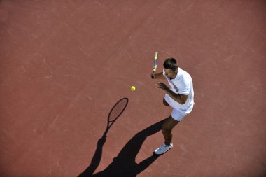 Young man play tennis outdoor on orange tennis field at early morning clipart