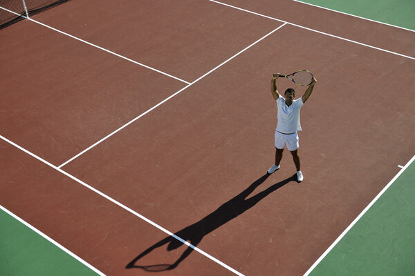 Молодой человек играет в теннис на открытом воздухе на оранжевом теннисном поле рано утром
