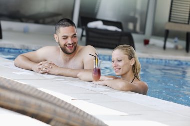 Happy young couple in love have fun relax and drink coctail at indoor wellness swimming pool clipart