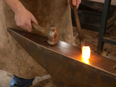 A blacksmith forging a horseshoe with a hammer onto anvil at the foreground. clipart