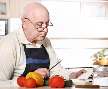 Senior man reading recipe from cookbook clipart