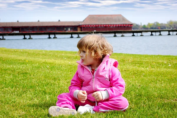 Little girl sitting on the shore of lake — Stock Photo, Image