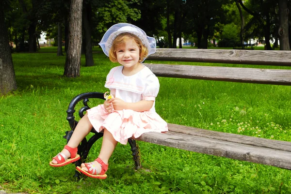 Kleines Mädchen sitzt auf Bank im Park — Stockfoto
