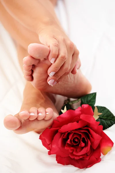 セクシーな女性の足および白い羽毛布団に赤いバラを手 — ストック写真