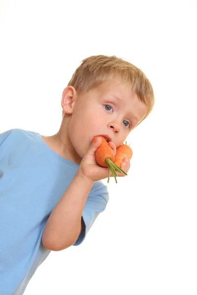 三岁男孩吃新鲜胡萝卜上白色隔离 图库照片