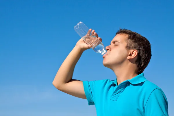 stock image Young male drinking water against blue sky