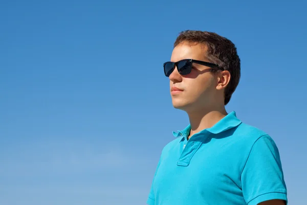 Allvarlig ung solglasögon mot blå himmel — Stockfoto