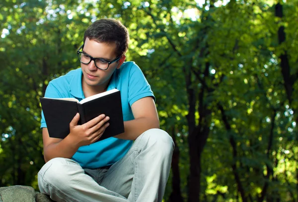 Młody człowiek czyta książkę w parku — Zdjęcie stockowe