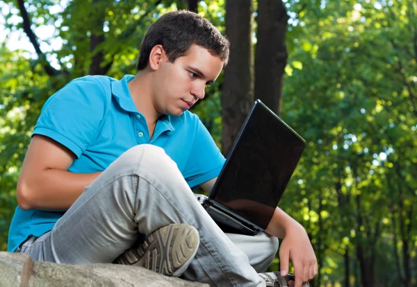 Молодой человек, работающий с ноутбуком в парке — стоковое фото