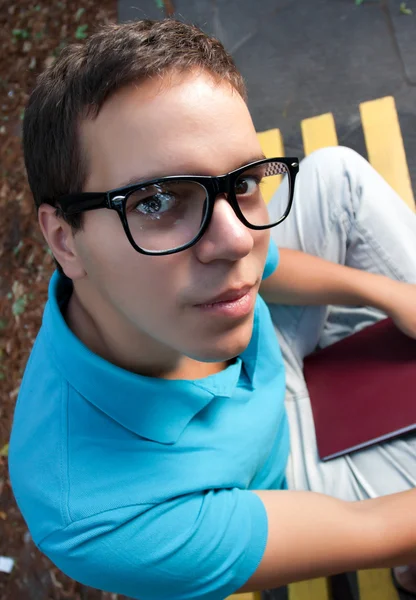 Wide angle portrait of young man in glasses sitting on a bench — Stock Photo, Image