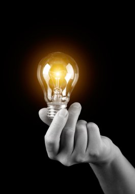 Hand holding light bulb isolated on black clipart