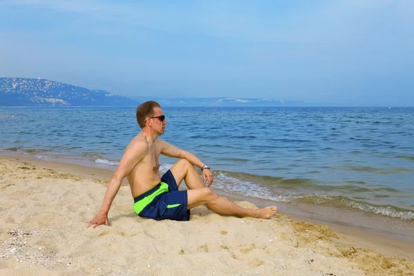 L'uomo siede in riva al mare e ha un riposo — Foto Stock