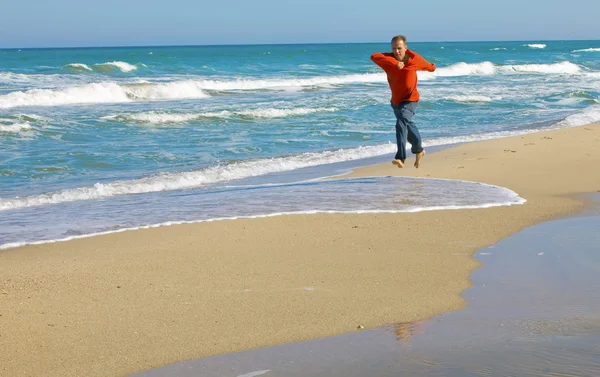 Man loopt in rode t-shirt op zand op seash — Stockfoto