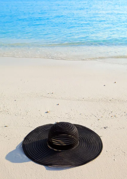 Μαύρη γυναικεία καπέλα από ήλιο ays στην άμμο πριν από τον ωκεανό — Φωτογραφία Αρχείου