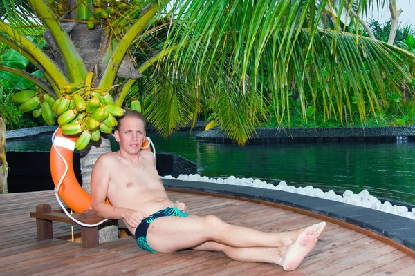 Young sports man under palm tree at pool. Maldives. — Stock Photo, Image