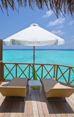 Parasol and chaise lounges on a terrace of water villa, Maldives. clipart