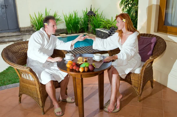 La pareja joven en el descanso romántico sobre la piscina detrás de la mesa con la fruta —  Fotos de Stock