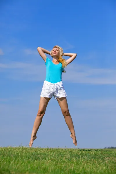 Mujer bastante joven saltando sobre hierba verde contra el cielo azul brillante —  Fotos de Stock