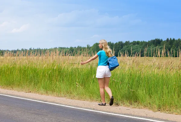 Beautiful young woman hitch hiking- in auto-stop "votes" on road — Stock Photo, Image