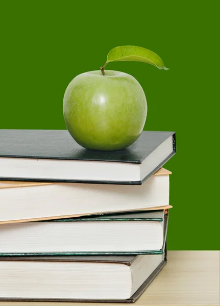 Manzana verde sobre pila de libros sobre fondo verde — Foto de Stock